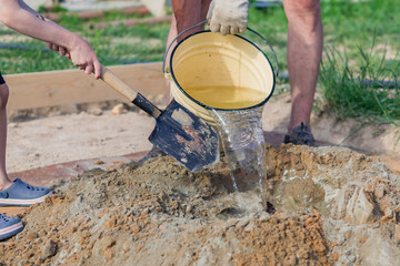 construction worker pooring water to the mixture of sand and cement. Making cement at construction...