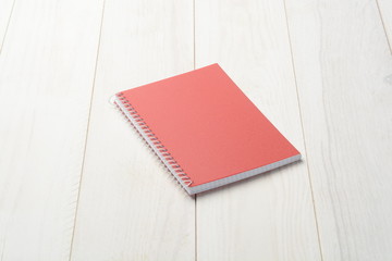 Cuaderno cerrado de tapa roja sobre fondo de madera blanca