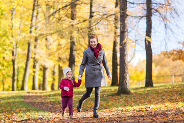family, season and people concept - happy mother and little daughter walking along autumn park