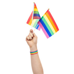 lgbt, same-sex relationships and homosexual concept - close up of male hand wearing gay pride awareness wristband holding rainbow flags