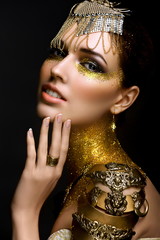 Portrait of Beautiful Woman with Golden Sparkles on her Face. Girl with Art Make-Up with Golden...