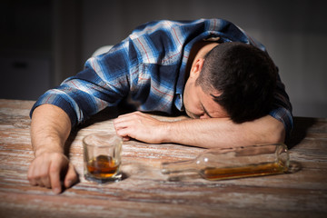 alcoholism, alcohol addiction and people concept - male alcoholic with glass of whiskey and bottle lying or sleeping on table at night
