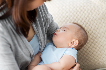 babyhood, childhood and people concept - close up of mother holding sleeping asian baby boy