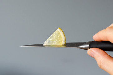 A piece of lemon on on a knife blade in hand. close-up