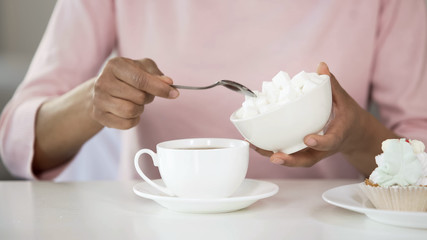 Female adding sugar in coffee, cake on table, diabetes risk, unhealthy food