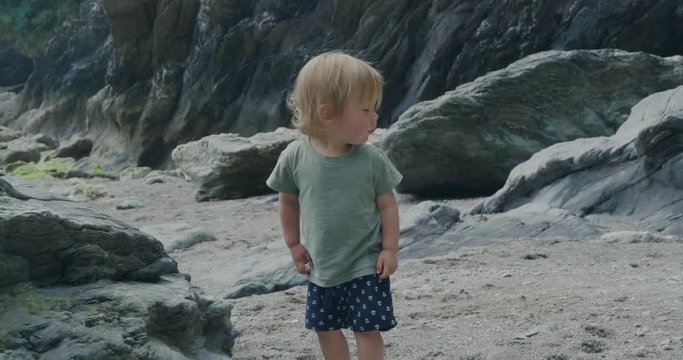 Little toddler boy walking on beach by rock face