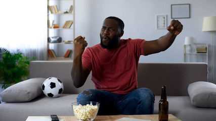 Happy afro-american man enjoying victory, watching sports competition on tv