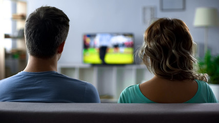Bored couple watching football match on tv, conflict, passive pastime together - Powered by Adobe