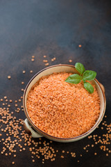 Bowl of raw split orange lentils on a brown metal background, vertical shot with space, elevated view