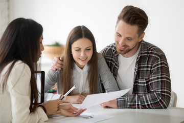 Female realtor showing house plan to excited millennial couple buying first property together, real...