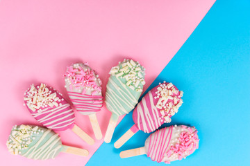 Different cake pops in form of popsicle on stick on pink and blue background.