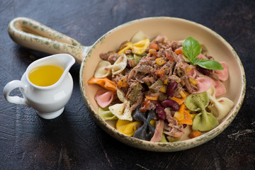 Serving pan with multicolored farfalle pasta and tuna fillet on a dark brown stone surface, studio shot, selective focus