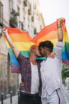 Gay couple holding gay pride flag kissing each other on the street 