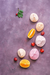 A variety of colorful meringue is beautifully located on a purple abstract background with strawberries, cherries and orange slices. Copy space, top view.