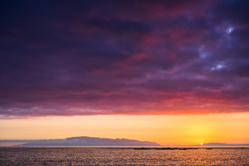 amazing scenic landscape taken during a wonerful sunset on the ocean. La Gomera oceanic island in background with clouds and water in red and orange colors. timeless moment with the sun going down 