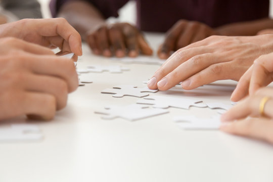Close up of diverse people hands assembling jigsaw puzzle together, multiethnic work team looking for business solution, showing unity, helping each other and cooperating. Teambuilding concept