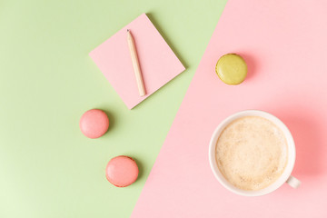 Cup of coffee with macaroons on pastel background.