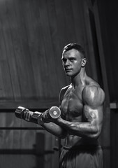 Fototapeta na wymiar Portrait of fit young muscular man working with dumbbells, black and white image