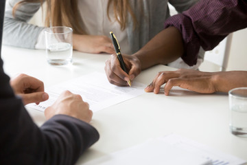 Close up of African American husband signing ownership contract buying first house with white wife,...