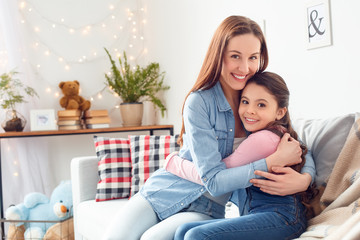 Obraz premium Mother and daughter at home sitting hugging looking camera joyful side view