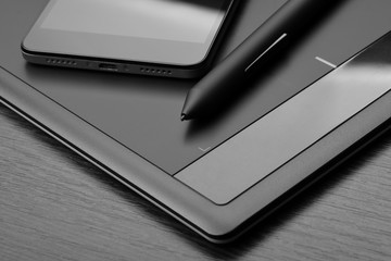 Smartphone and digitizer (digital drawing tablet) with a special pen-like stylus on a wooden table....