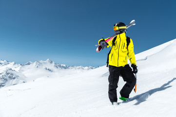 Fototapeta na wymiar A portrait of a skier in a protective helmet and glasses is a mask and scarf with skis on his shoulder in the snow-capped mountains of the Caucasus. Skiing,