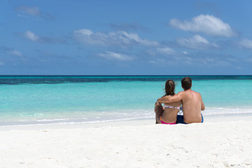 Fototapeta na wymiar Verliebtes junges Paar sitzend an weißem Sandstrand Blick zum Meer