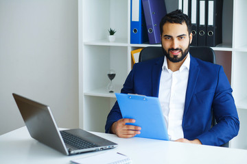 Office Business Man in a Light Office with Big Windows Holding a Blue Folder in Hand. Man Dressed in Blue Costume and White Shirt. High Resolution