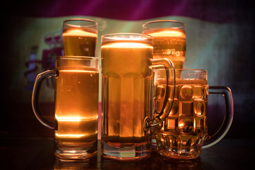 Creative concept. Beer glasses on table at dark toned foggy background with blurred view of flag of Spain. Support your country with beer concept