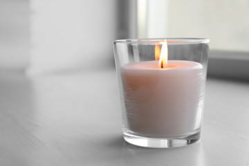 Beautiful burning wax candle in glass on table