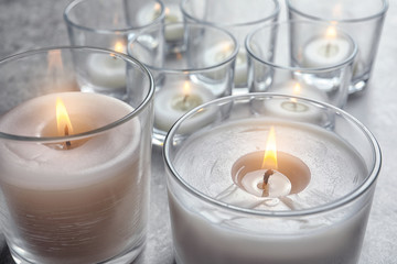Obraz na płótnie Canvas Burning wax candles in glasses on table, closeup