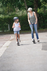 Fototapeta premium Mother and daughter riding scooters in the street