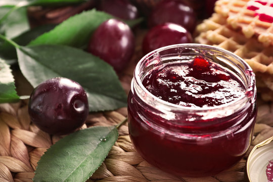 Small glass jar with tasty homemade plum jam on wicker mat