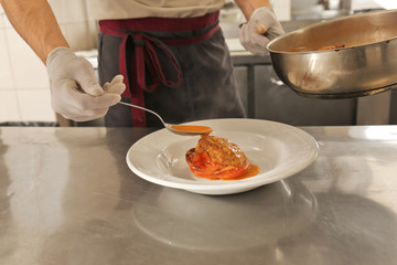 Male chef pouring sauce onto meat in restaurant kitchen