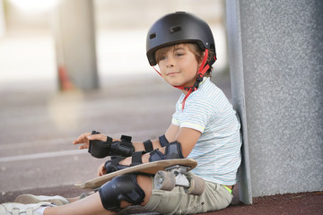 Young boy with skateboard sitting on the ground © goodluz