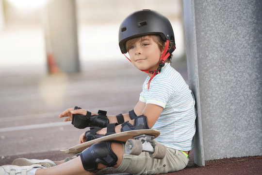 Young boy with skateboard sitting on the ground