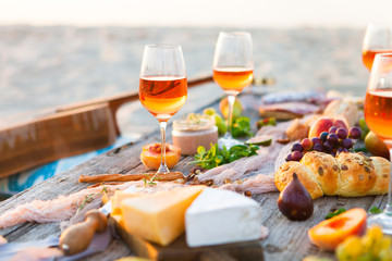 Picnic on beach at sunset in boho style. Romantic dinner, friends party, summertime, food and drink concept - 211170343