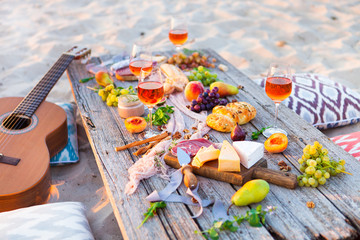 Picnic on beach at sunset in boho style. Romantic dinner, friends party, summertime, food and drink concept