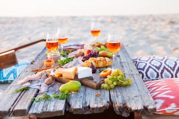 Picnic on beach at sunset in boho style. Romantic dinner, friends party, summertime, food and drink concept