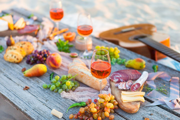 Picnic on beach at sunset in boho style. Romantic dinner, friends party, summertime, food and drink concept - 211170375