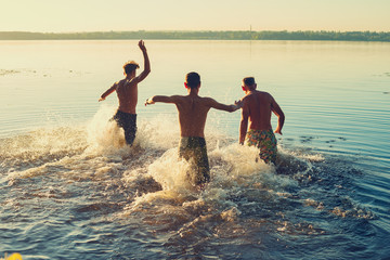 Joyful friends run into the water in a cloud of spray