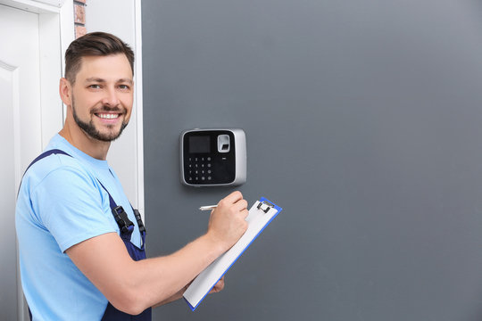 Male technician with clipboard near installed alarm system indoors