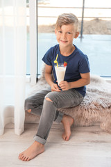 Little boy with glass of milk shake near window indoors