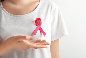 Woman with pink ribbon on t-shirt against light background. Cancer awareness