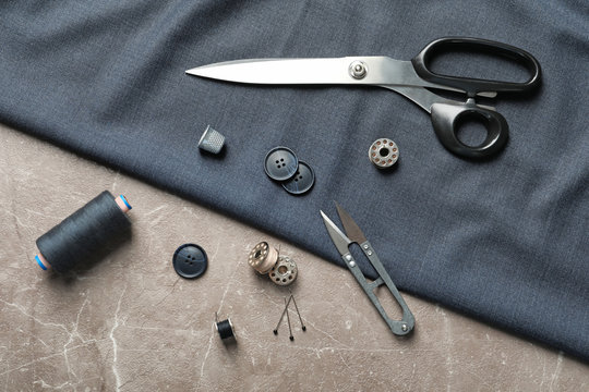 Set of tailoring accessories and fabric on grey background, top view