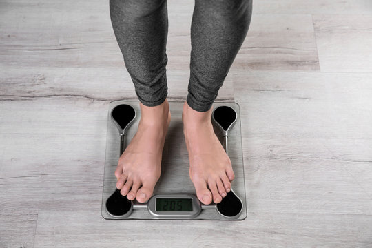 Young woman measuring her weight using scales on floor, top view. Weight loss motivation