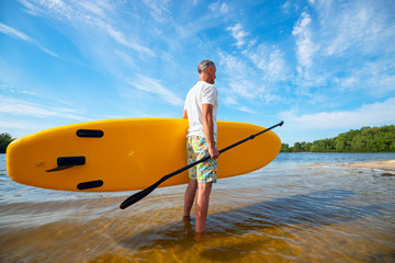 Man is standing with a SUP board and a paddle in his hands