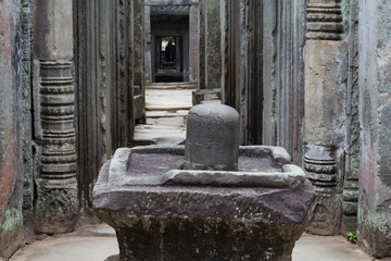 Ancient stone ruin in Angkor Wat temple. Stone lingam in decorated gallery. Khmer heritage temple ruin in jungle.