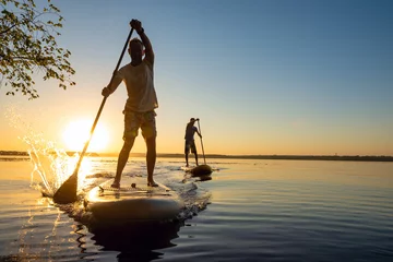 Fotobehang Men, friends sail on a SUP boards in a rays of rising sun © sanechka