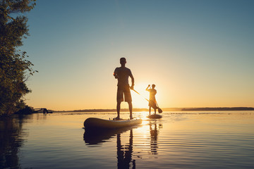 Men, friends sail on a SUP boards in a rays of rising sun